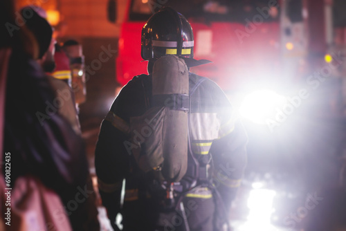 Group of fire men in protective uniform during fire fighting operation in the night city streets, firefighters brigade with the fire engine truck vehicle, emergency and rescue service