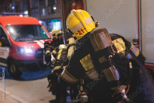 Group of fire men in protective uniform during fire fighting operation in the night city streets, firefighters brigade with the fire engine truck vehicle, emergency and rescue service photo