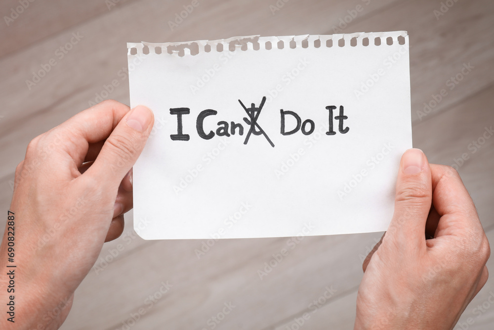 Motivation concept. Woman holding paper with changed phrase from I Can't Do It into I Can Do It by crossing over letter T indoors, closeup Motivation concept. Woman holding paper with changed phrase from I Can't Do It into I Can Do It by crossing over letter T indoors, closeup
