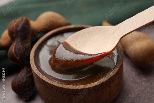 Taking tasty tamarind sauce with spoon from bowl on brown table, closeup photo
