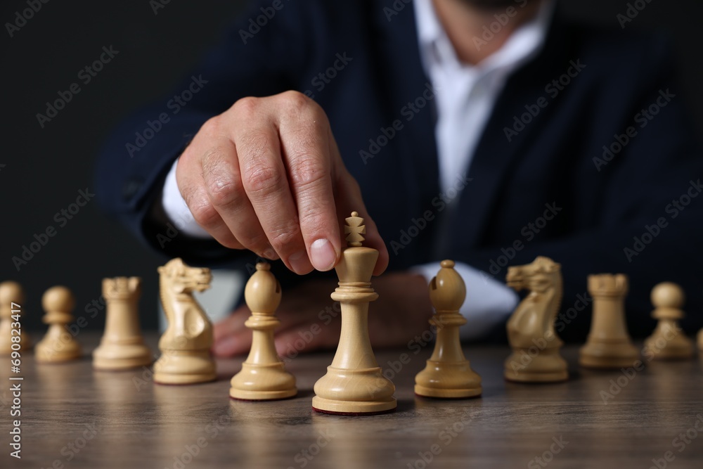 Man with chess pieces at wooden table against dark background, closeup Man with chess pieces at wooden table against dark background, closeup