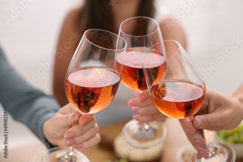 People clinking glasses with rose wine indoors, closeup