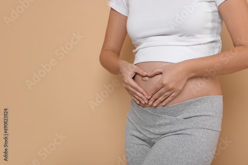Pregnant woman making heart with hands on beige background, closeup. Space for text