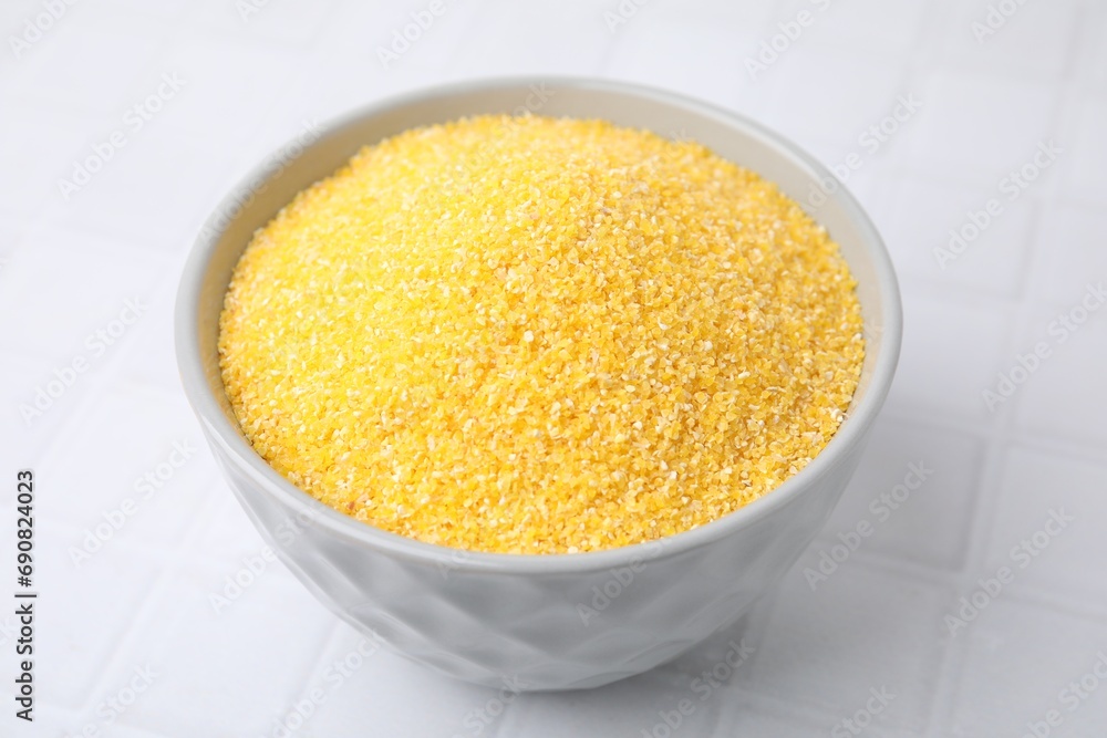 Raw cornmeal in bowl on white tiled table, closeup Raw cornmeal in bowl on white tiled table, closeup