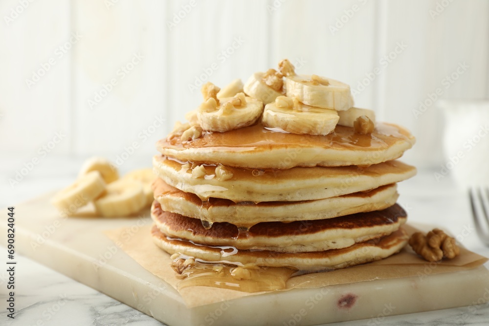 Delicious pancakes with bananas, walnuts and honey on white marble table, closeup