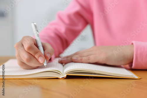 Young woman writing in notebook at wooden table, closeup