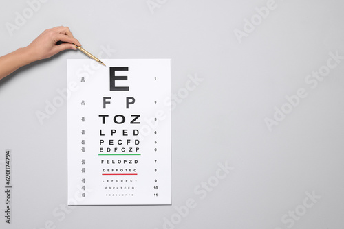 Ophthalmologist pointing at vision test chart on gray background, closeup. Space for text