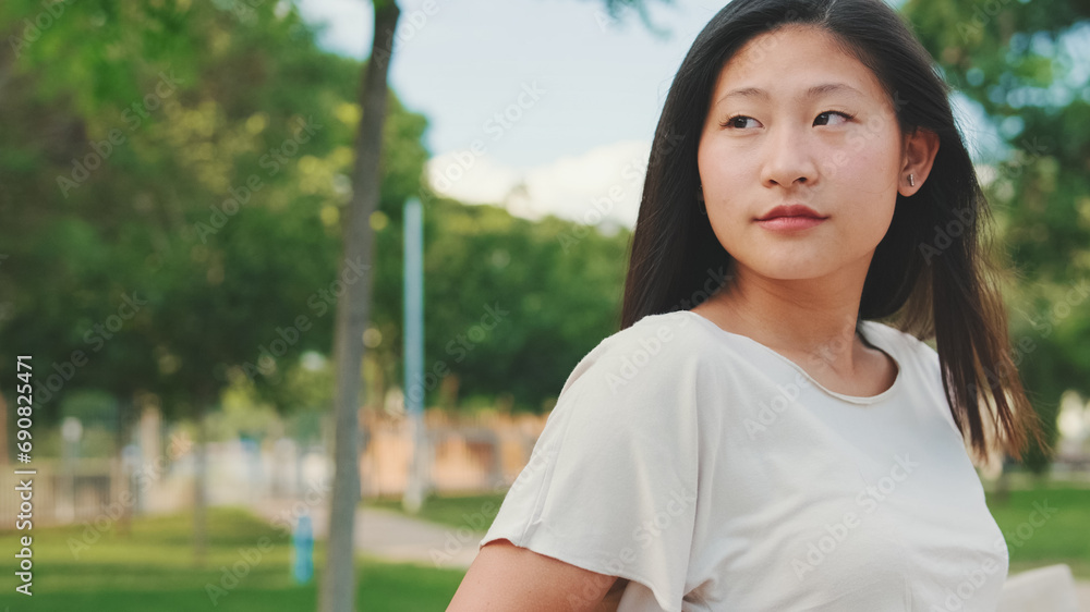 Beautiful brunette girl is resting sitting on bench in city park, looking around Beautiful brunette girl is resting sitting on bench in city park, looking around