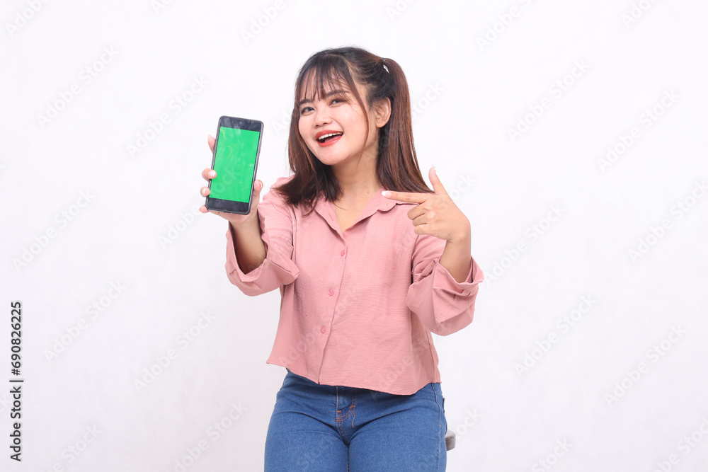Beautiful happy Asian woman in her 20s wearing casual shirt holding green screen cell phone laughing pointing at gadget on white background studio portrait for banner ad, banner, billboard Beautiful happy Asian woman in her 20s wearing casual shirt holding green screen cell phone laughing pointing at gadget on white background studio portrait for banner ad, banner, billboard