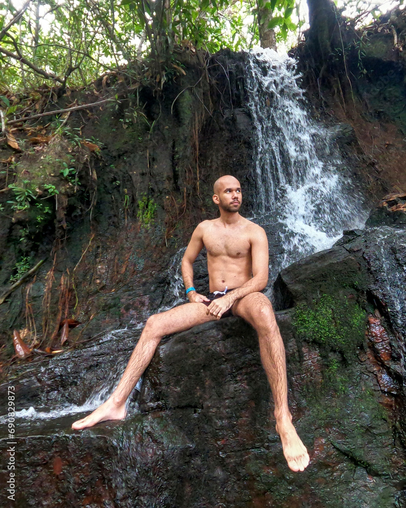 Slim man in swimming trunks sitting under the waterfall, Alto Paraíso de Goiás, GO, 2023 Slim man in swimming trunks sitting under the waterfall, Alto Paraíso de Goiás, GO, 2023