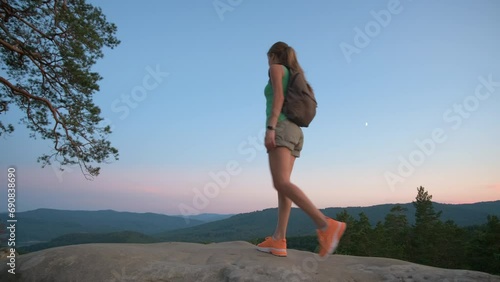 Wallpaper Mural Sportive woman walking alone on hillside trail. Female hiker enjoying view of evening nature from rocky cliff on wilderness path. Active lifestyle concept Torontodigital.ca