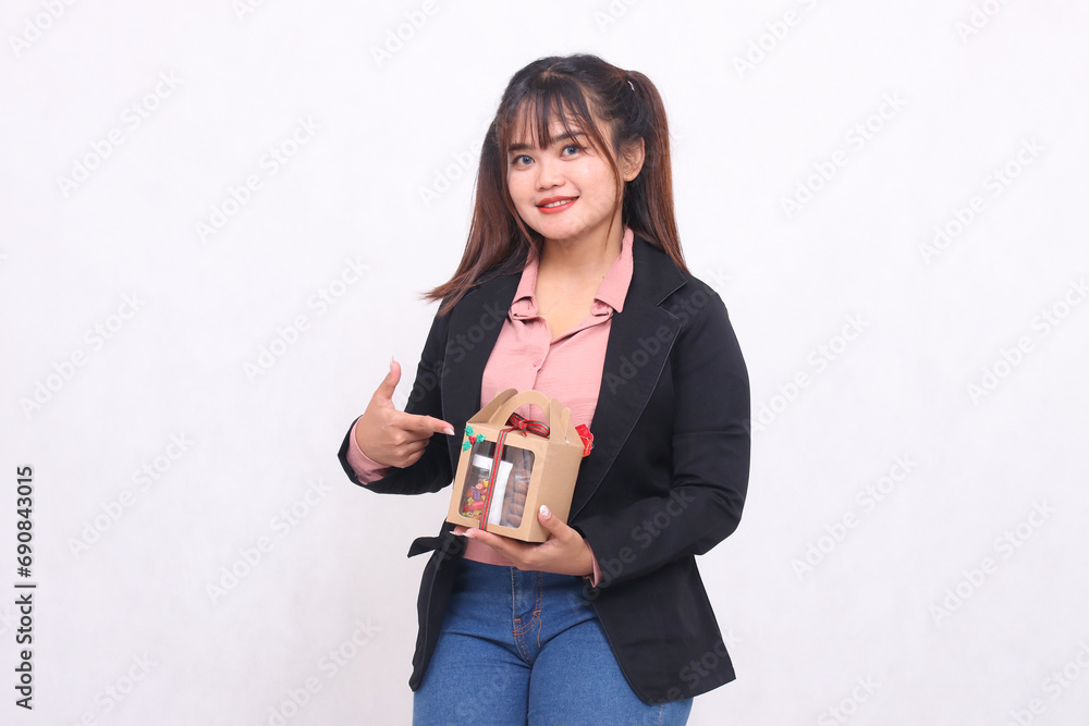 Beautiful Asian girl in her 20s smiling excitedly pointing to Christmas gift in the form of hamper in hand on white background for advertising materials, banners, billboards Beautiful Asian girl in her 20s smiling excitedly pointing to Christmas gift in the form of hamper in hand on white background for advertising materials, banners, billboards