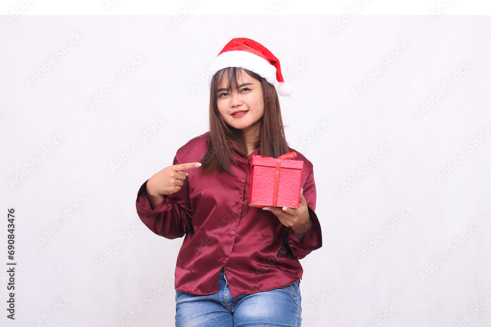 Photo portrait of a beautiful elegant Asian girl in her 20s carrying boxed gifts at Christmas Santa Claus hat wearing shiny modern red shirt showing gifts on a white background for promotion Photo portrait of a beautiful elegant Asian girl in her 20s carrying boxed gifts at Christmas Santa Claus hat wearing shiny modern red shirt showing gifts on a white background for promotion