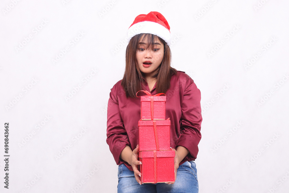 beautiful young southeast asian girl surprised carrying 3 boxes of gifts at christmas wearing santa claus hat modern red shirt outfit looking at boxes all white background for promotion beautiful young southeast asian girl surprised carrying 3 boxes of gifts at christmas wearing santa claus hat modern red shirt outfit looking at boxes all white background for promotion