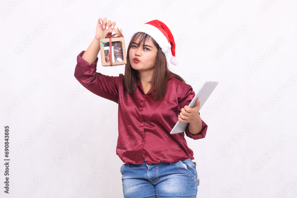 beautiful young southeast asian woman kissing food package gift in hamper and laptop tablet in christmas wearing santa hat modern red shirt outfit white background for promotion and advertising beautiful young southeast asian woman kissing food package gift in hamper and laptop tablet in christmas wearing santa hat modern red shirt outfit white background for promotion and advertising