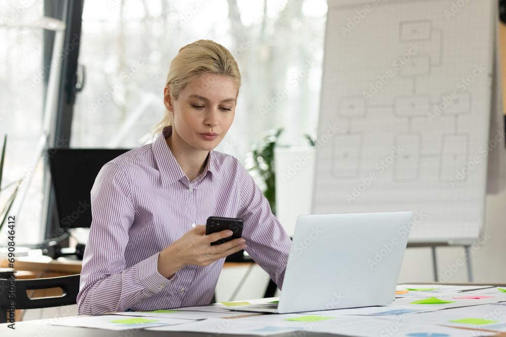 Focused young Caucasian female employee work on computer texting messaging on smartphone. Concentrated millennial businesswoman use laptop consult client or customer online on cellphone. Focused young Caucasian female employee work on computer texting messaging on smartphone. Concentrated millennial businesswoman use laptop consult client or customer online on cellphone.