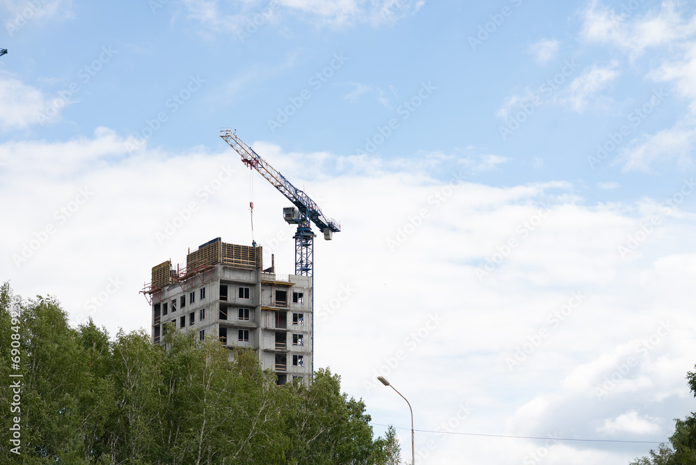 View of the unfinished wall of the house. A construction crane on a blue sky background.