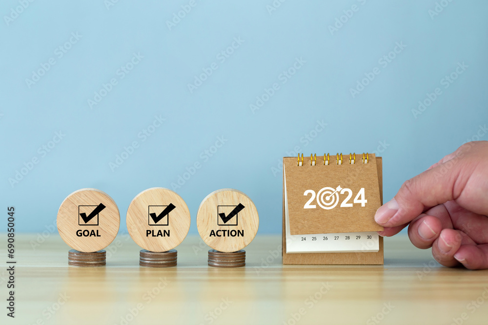 Happy New Year 2024 banner background. 2024 numbers year with target dart icon on desk calendar with hand turns over a calendar sheet.  Goal, Plan, Action on wooden cube. Business goals plan action. - obrazy, fototapety, plakaty 