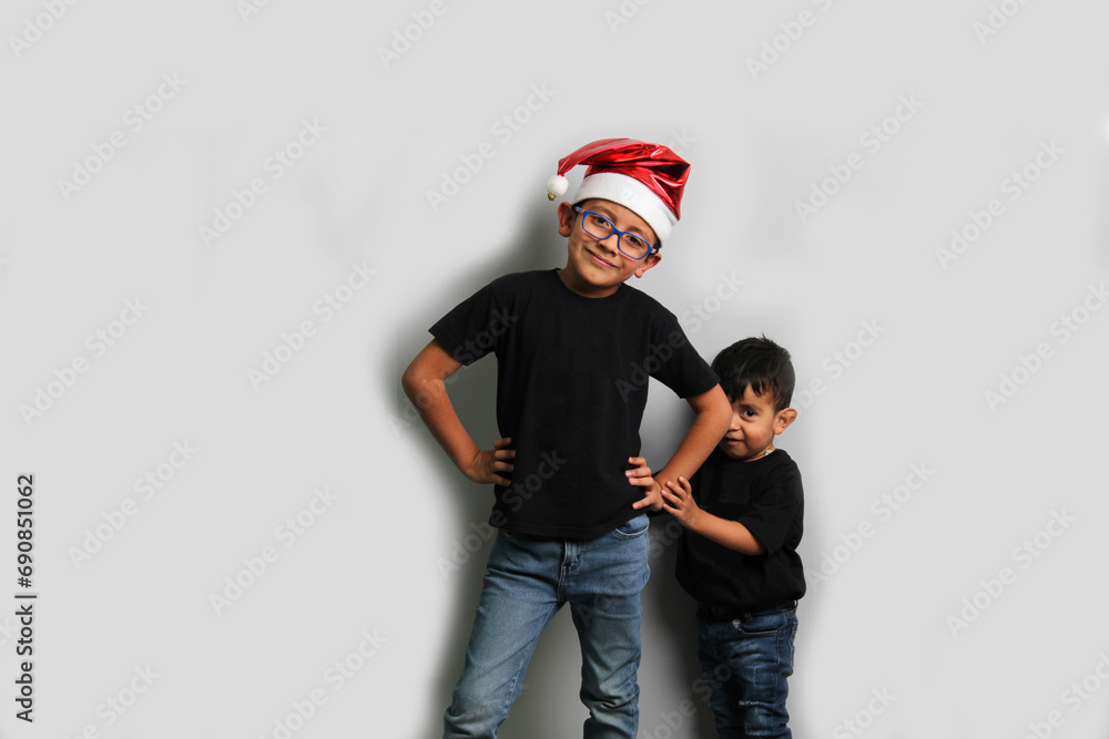 Fototapeta premium Dark-skinned Latino children, older brother in Santa hat takes care of his younger brother and spends quality time at the holidays to celebrate Christmas