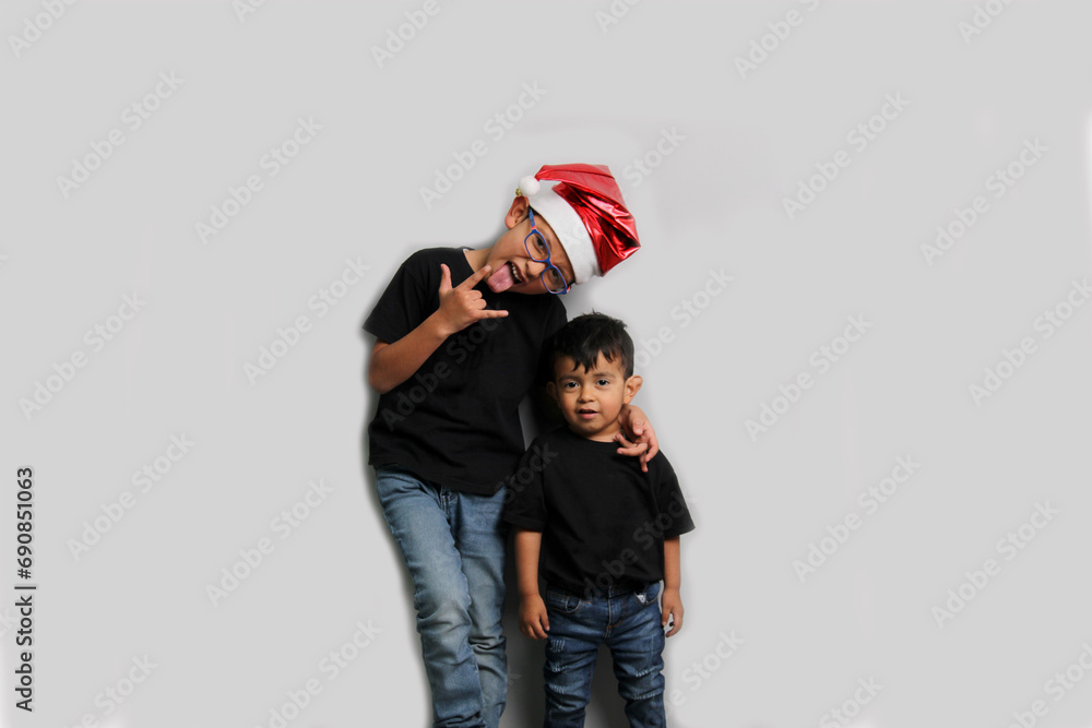 Dark-skinned Latino children, older brother in Santa hat takes care of his younger brother and spends quality time at the holidays to celebrate Christmas Dark-skinned Latino children, older brother in Santa hat takes care of his younger brother and spends quality time at the holidays to celebrate Christmas