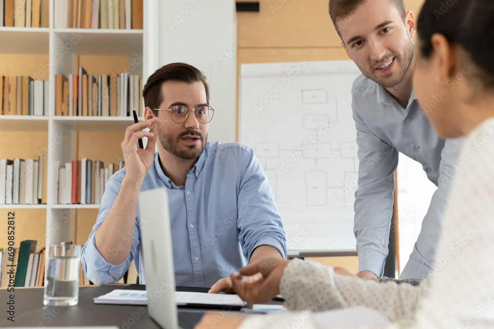 Obraz premium Multiracial businesspeople gather at desk in office brainstorm over business project together. Motivated diverse colleagues talk discuss ideas at meeting or briefing. Teamwork, collaboration concept.