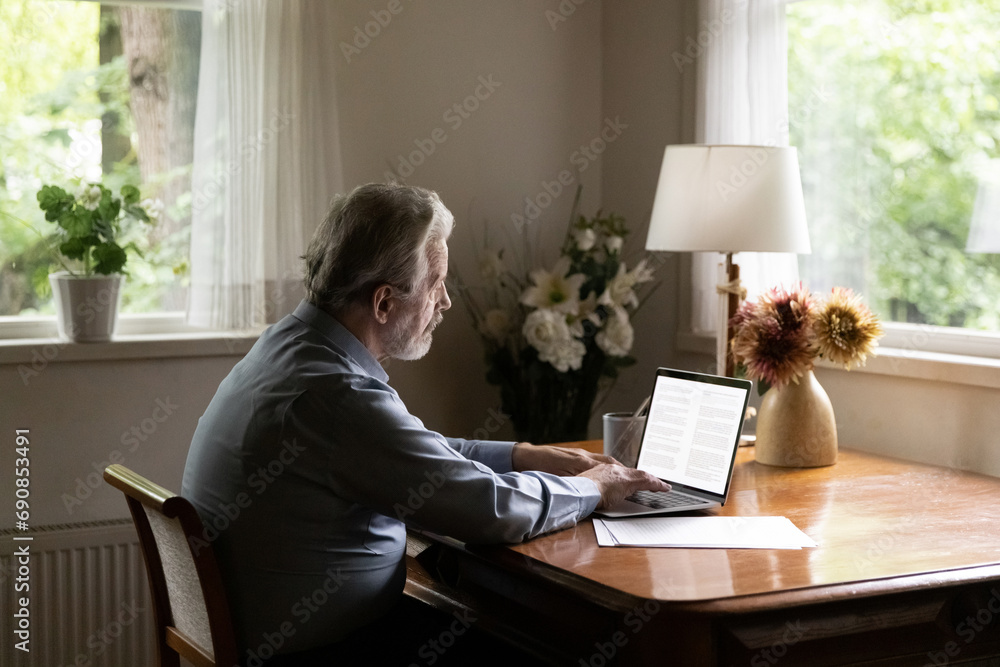 Aged person and tech. Mature grey haired man writer working on book typing text on laptop at cozy home office. Senior elderly male pensioner using pc to write email search information browse websites Aged person and tech. Mature grey haired man writer working on book typing text on laptop at cozy home office. Senior elderly male pensioner using pc to write email search information browse websites
