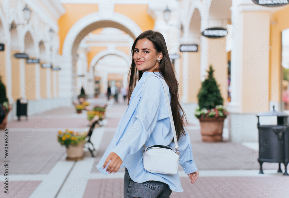 Attractive caucasian girl in casual clothes looks back at camera walks outside goes to shopping, sales, discount, promo.Women fashion, summertime.