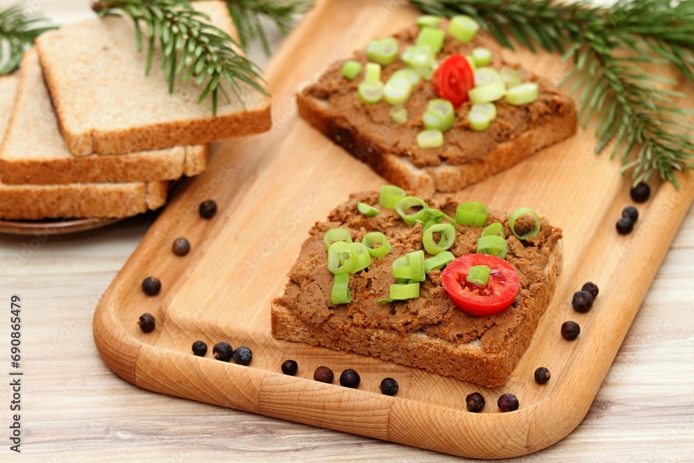 Pate spread from deer meat on whole grain bread and green onion. Sandwich with meat pate on cutting board, fresh tomatoes and spices for venison around. Decorated with spruce branch. Pate spread from deer meat on whole grain bread and green onion. Sandwich with meat pate on cutting board, fresh tomatoes and spices for venison around. Decorated with spruce branch.