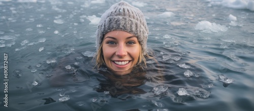 Young woman smiling while swimming in a frozen lake's ice hole, wearing a gray hat and gloves.