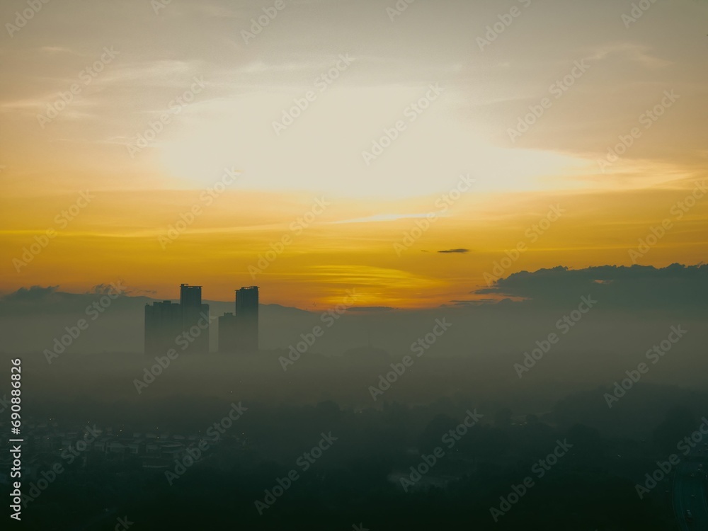 An aerial view of the misty morning fog and a golden sunrise near a neighborhood in Malaysia. An aerial view of the misty morning fog and a golden sunrise near a neighborhood in Malaysia.