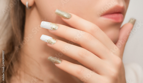 Female hands with long nails with glitter nail polish. Long gold nails near face. Stylish fashion manicure.
