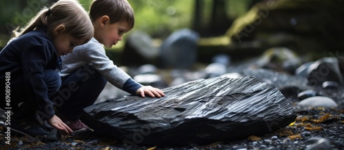 Child exploring dark grey shale slate natural rock fossil in forest with family. photo