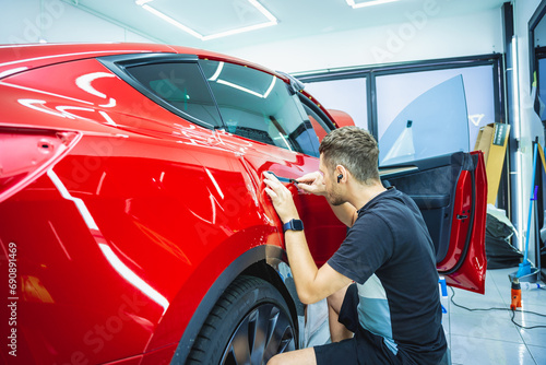 The process of installing protective film on the new red car.