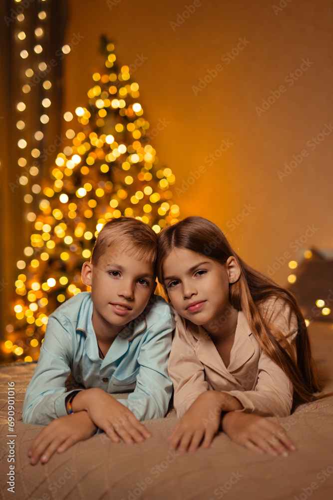Twins boy and girl, brother and sister, at home waiting for the New Year holiday in the bedroom on the bed