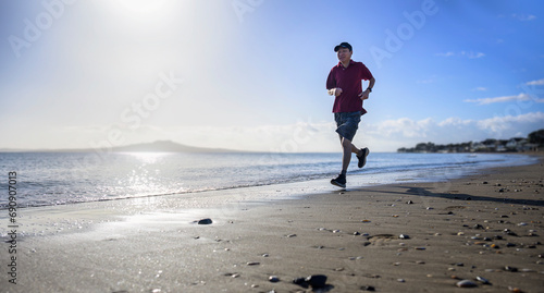 Man running on the beach in the morning. Front view. Milford beach. Auckland.