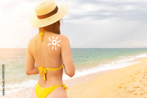 Sexy woman in bikini with sunscreen on her skin. The beauty took care of her tan and applied sun-shaped cream to her shoulder