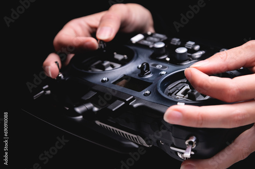 Close-up view of a woman operating the remote control of an FPV racing drone. Hands holding black fpv drone transmitter, on black background photo