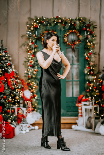 Portrait of a wealthy mature woman with evening make-up and hairstyle posing in a black dress on the background of the Christmas room. Luxurious lifestyle. Christmas holidays concept