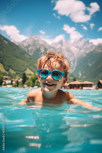 child in sunglasses in the pool against the background of the mountains © Anna