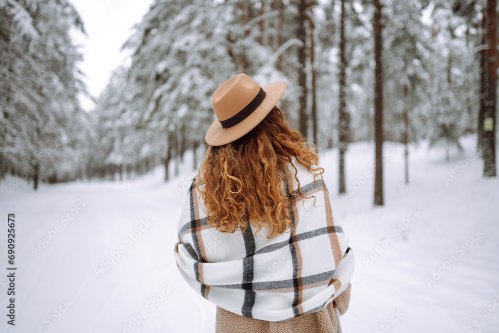 Fototapeta premium Beautiful woman posing with her back in the winter forest. Great winter weather and atmosphere. She is dressed in a winter coat, hat and scarf. Happy winter time. Christmas.