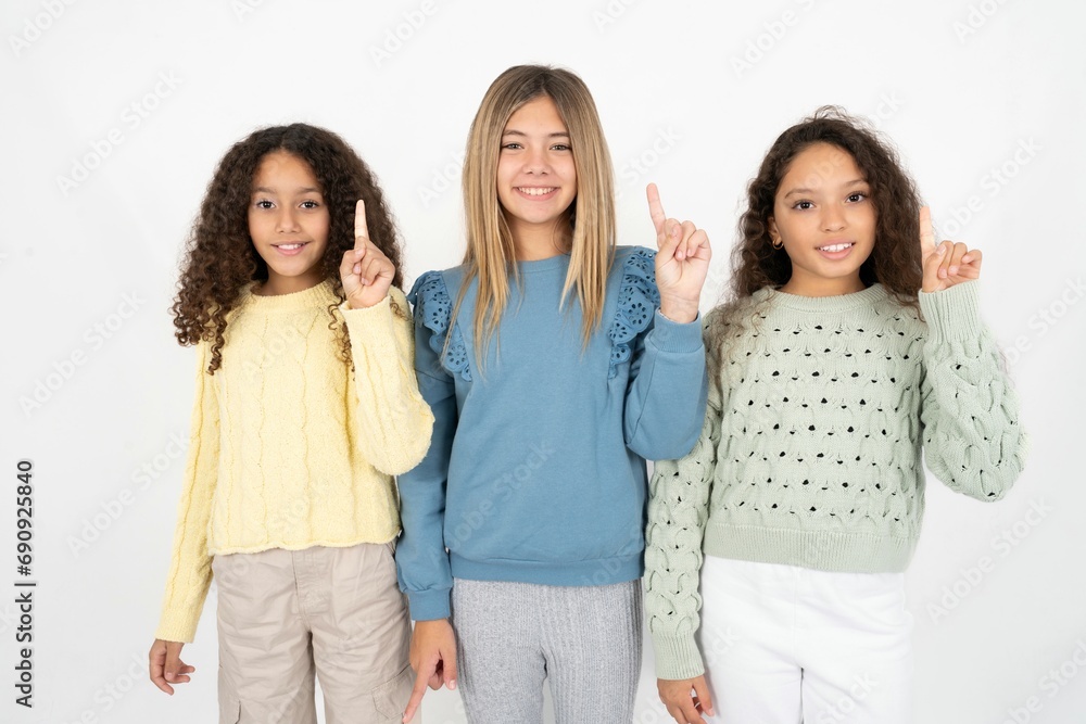 Three beautiful multiracial kid girls showing and pointing up with finger number one while smiling confident and happy. Three beautiful multiracial kid girls showing and pointing up with finger number one while smiling confident and happy.