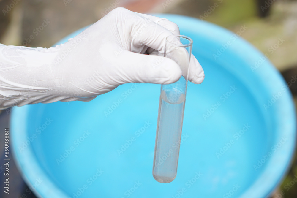 Close up ecologist hand wears glove holds test tube of water. Concept, Inspecting water quality from nature source that use in daily life. Examination water pollution. Environmental problems. Close up ecologist hand wears glove holds test tube of water. Concept, Inspecting water quality from nature source that use in daily life. Examination water pollution. Environmental problems.