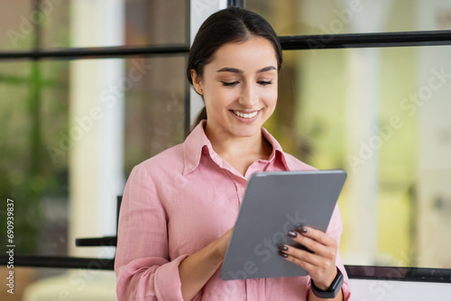 Smiling millennial arab woman manager typing on tablet, chatting in coworking office
