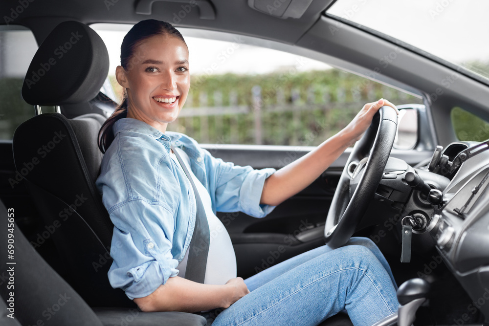 Cheerful pregnant woman sits confidently in driver's seat in automobile Cheerful pregnant woman sits confidently in driver's seat in automobile