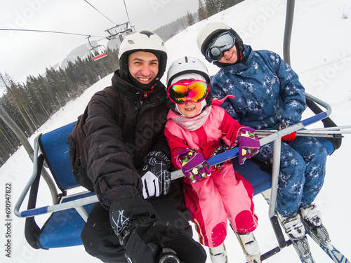 Skiing, ski lift, ski resort - happy smiling family skiers on ski lift making selfie