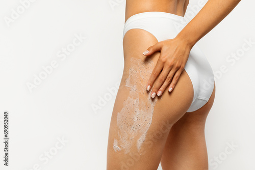 Close up view of woman applying thick layer of exfoliating body scrub on thigh photo