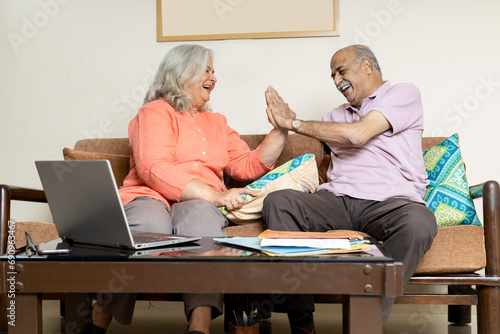 Overjoyed indian senior couple happily living retirement life, senior couple doing high five while sitting on sofa at living room