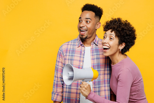 Young couple two friend family man woman of African American ethnicity in casual clothes together scream in megaphone announces discounts sale Hurry up look aside isolated on plain yellow background