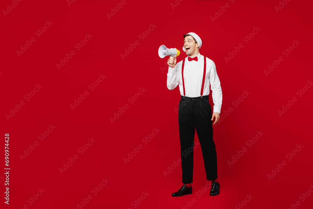 Full body merry young man wear white shirt Santa hat posing scream in megaphone announces discounts sale Hurry up isolated on plain red background Happy New Year Christmas celebration holiday concept Full body merry young man wear white shirt Santa hat posing scream in megaphone announces discounts sale Hurry up isolated on plain red background Happy New Year Christmas celebration holiday concept