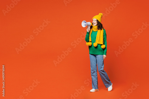 Full body young woman she wear green knitted sweater yellow hat scarf hold in hand megaphone scream announces discounts sale Hurry up isolated on plain orange red background studio. Lifestyle concept.